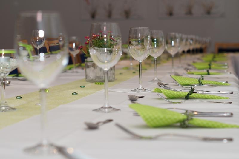 Gedeckter Tisch mit Besteck, Gläsern und grünen Servietten.