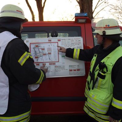 Das Bild zeigt den Einsatzleiter der Feuerwehr bei der Unterweisung eines Abschnittseinsatzleiters an einem taktischen Einsatzstellenplan.