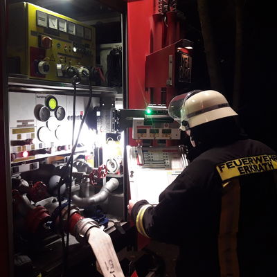 Das Bild zeigt einen Feuerwehrmann bei der Atemschutzüberwachung und seiner Tätigkeit als Maschinist am Pumpenbedienstand des Hilfeleistungslöschfahrzeuges.