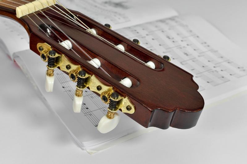 Gitarrenkopf in Nahaufnahme mit darunterliegenden Noten auf Papier
