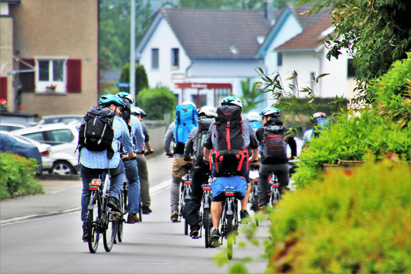 Eine Gruppe Männer mit Rucksäcken fährt auf Fahrrädern auf der Straße.