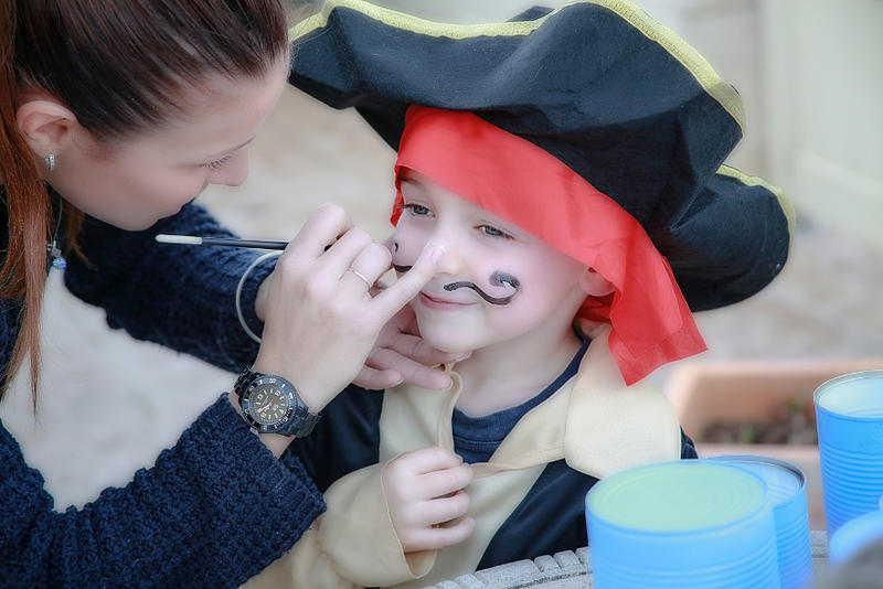Eine Frau schminkt einen kleinen, verkleideten Jungen als Pirat.