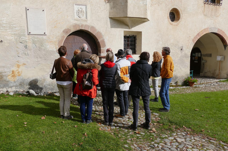 Eine Gruppe Besucher hört den Erklärungen eines Museumsmitarbeiters an einer historischen Außenmauer zu.