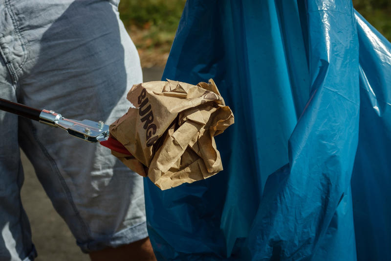 Eine leere Fastfood-Tüte wird mit einer Greifzange in einen blauen Müllsack gelegt.