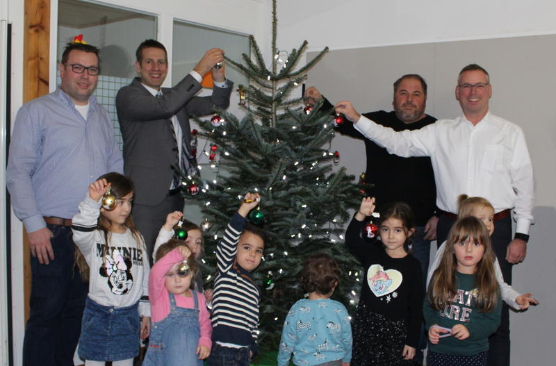 Tobias Wagemann, Bürgermeister Christoph Schultz, Syla Zabeli und Andre Kowalczyk schmücken gemeinsam mit den Kindern der Kindertagestätte am Schimmelskämpchen einen Tannenbaum.