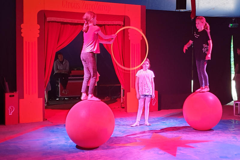 Zwei Mädchen auf Bällen proben im Circus ZappZarap eine Jonglage-Nummer.