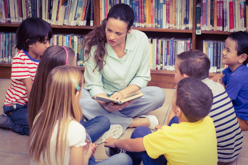 Eine Frau liest Kindern in der Bibliothek aus einem Kinderbuch vor.