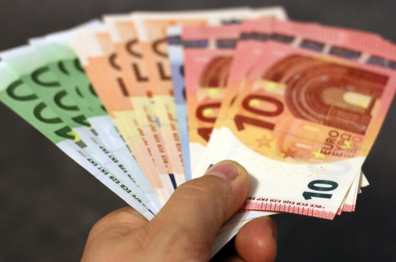 Das Bild zeigt, wie eine Hand mehrere Euro-Geldscheine entgegenstreckt.