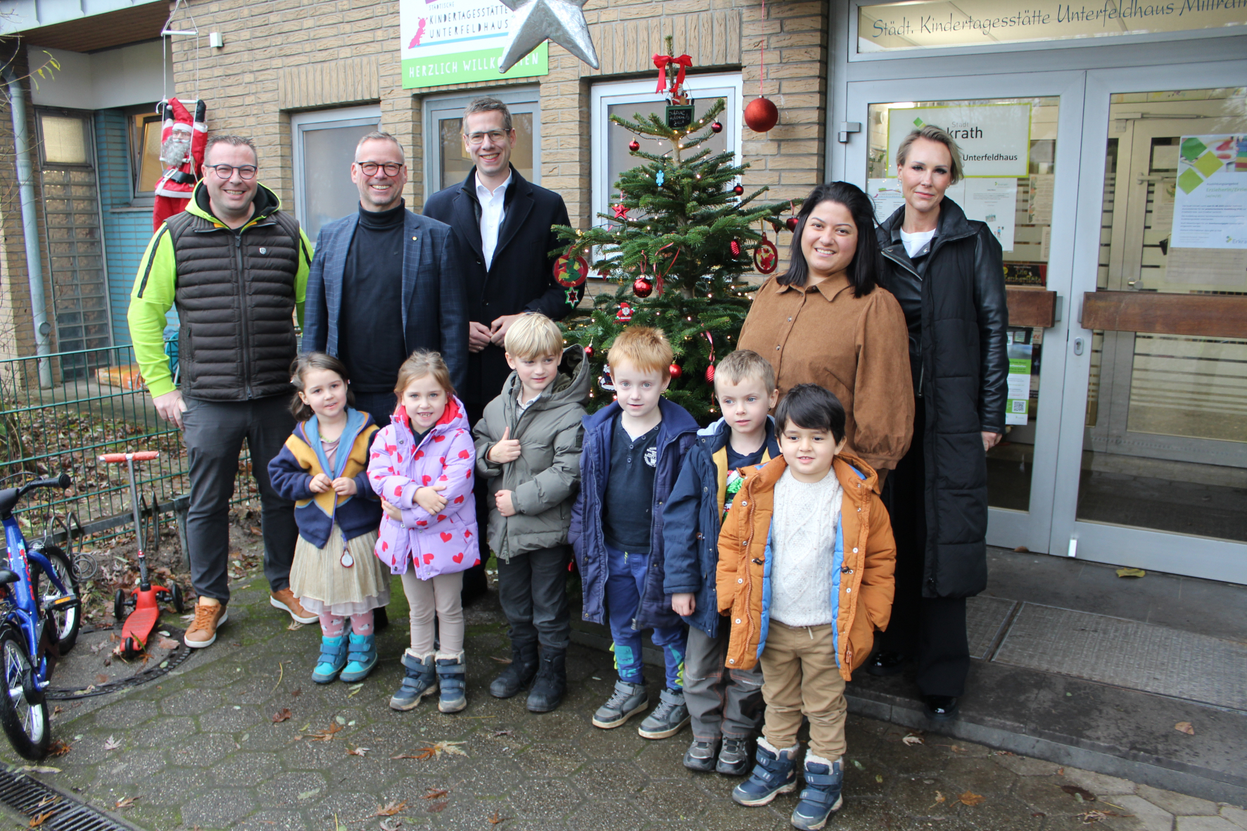 Kindergartenkinder stehen vor einem geschmückten Tannenbaum und erwachsenen Menschen.