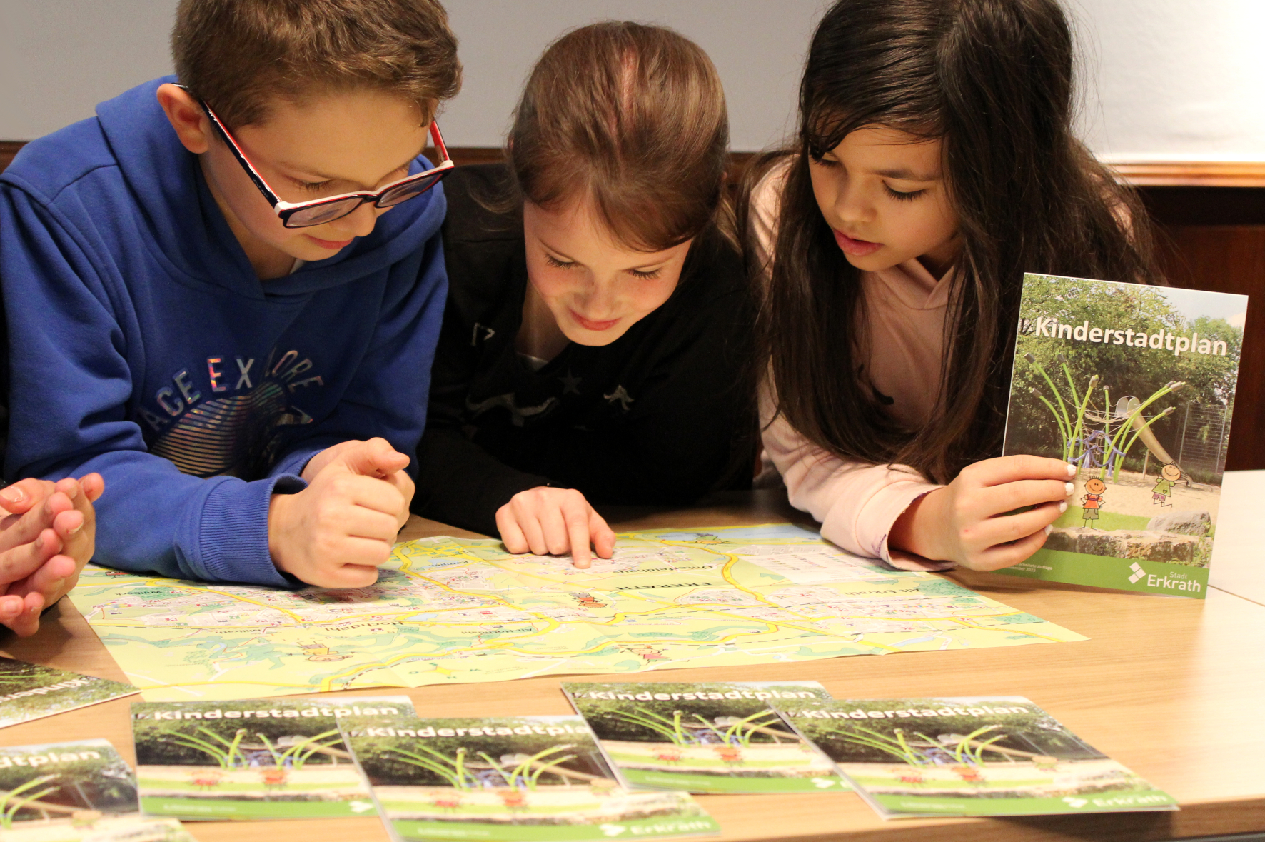 Zwei Mädchen und ein Junge schauen in den Kinderstadtplan der Stadt Erkrath.