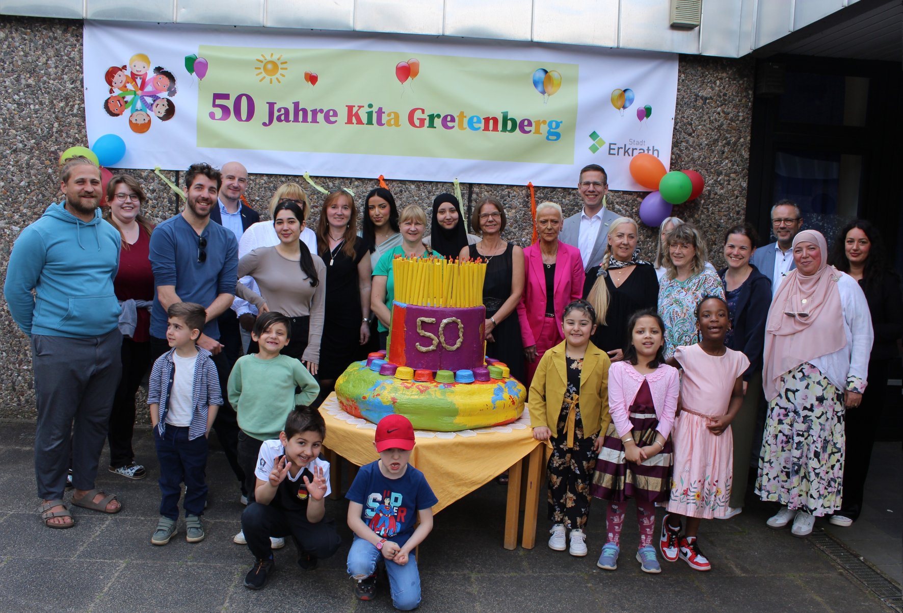 Kinder und Erwachsene feiern mit einer großen bunten Tortenskulptur 50-jähriges Bestehen der Kita Gretenberg