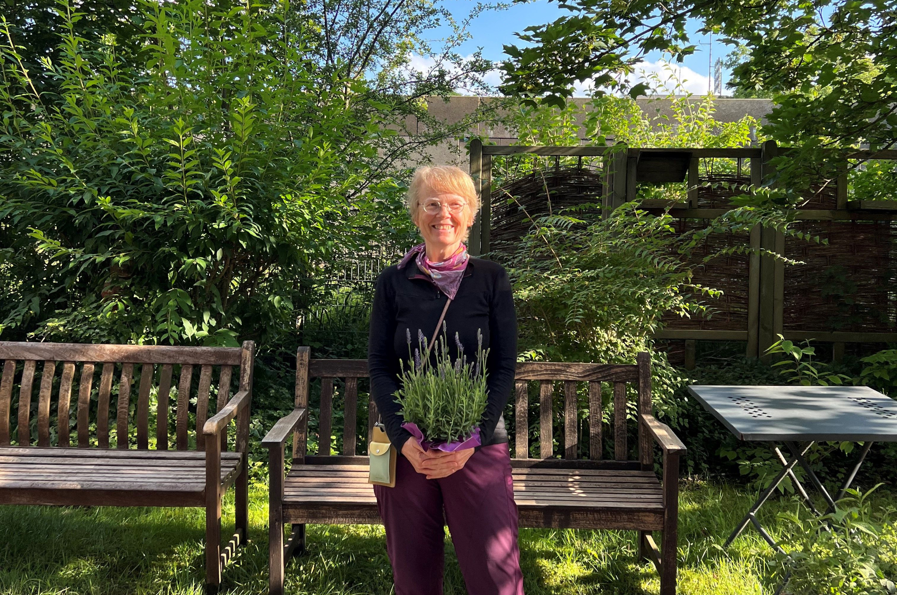 Anemone Hansen mit einem Lavendel in der Hand vor einer Holzbank