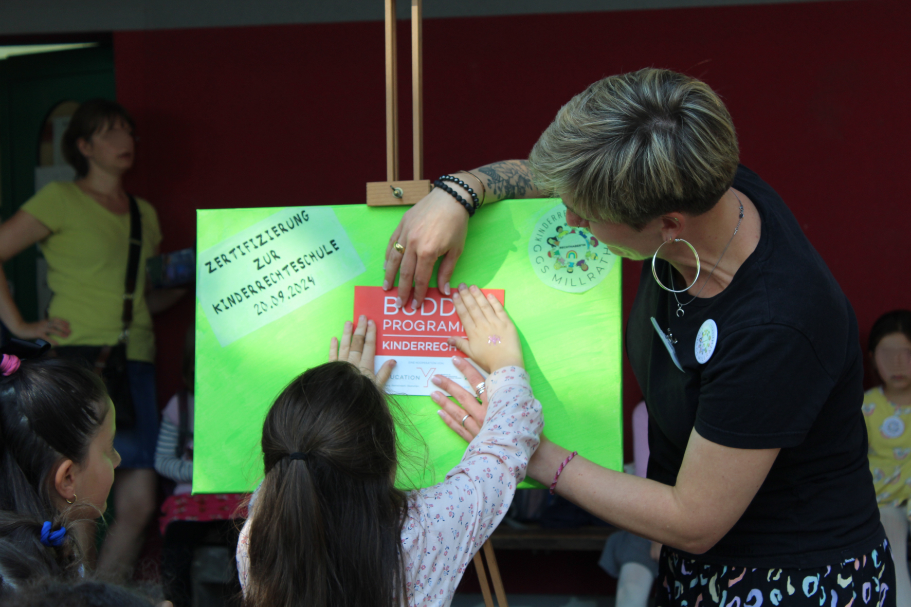 Zertifizierung zur Kinderrechtsschule wird als Aufkleber an grüner Leinwand von einem Kind angeklebt