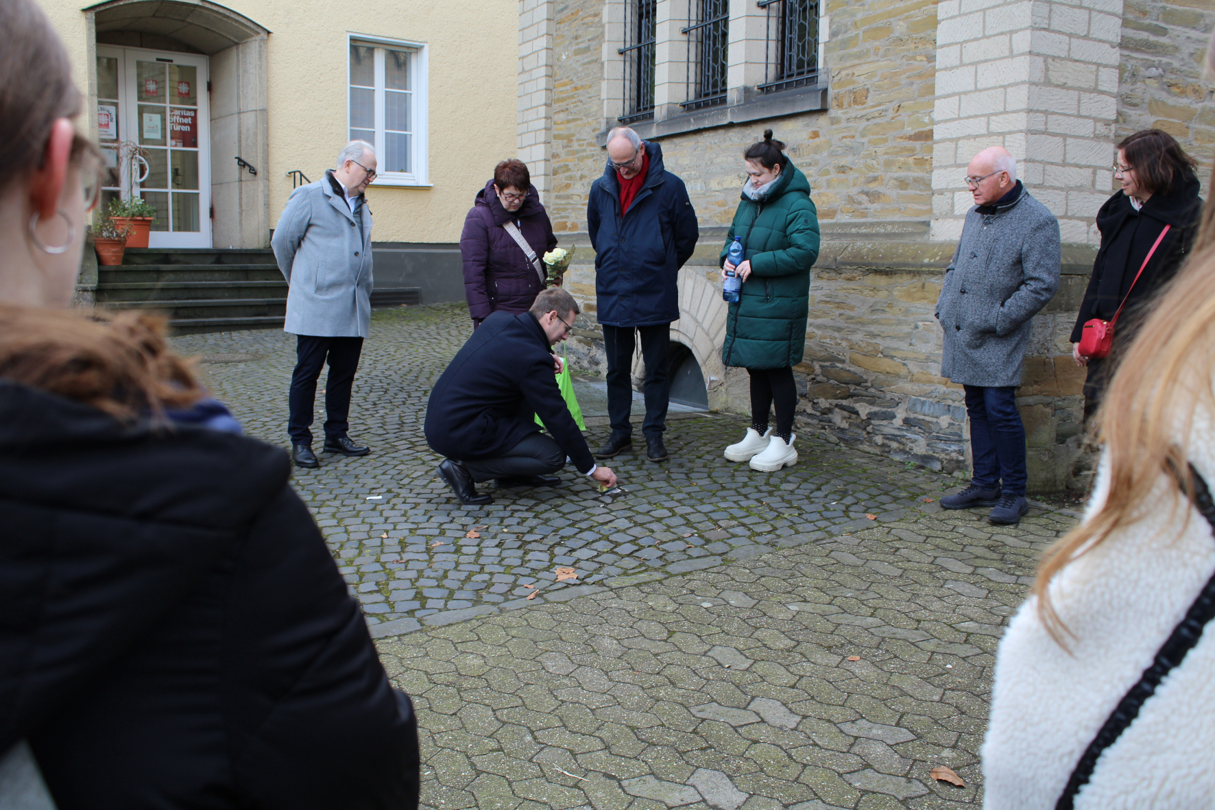 Bürgermeister Christoph Schultz und Mitglieder der Ratsparteien reinigen einen Stolperstein in Erkrath.