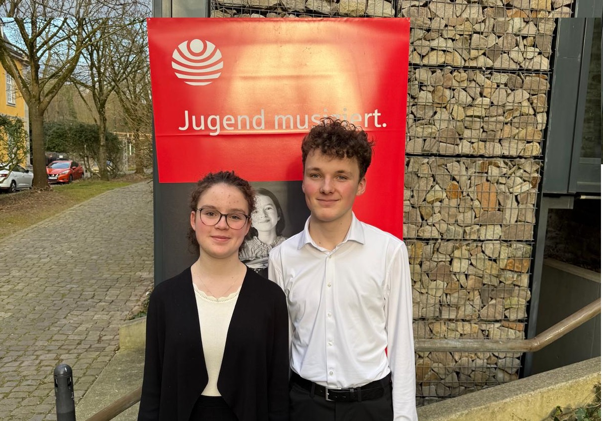 Die Geschwister Sophia und Jonas Amelingmeyer stehen vor einem Banner des Landeswettbewerb „Jugend musiziert“ in Essen.