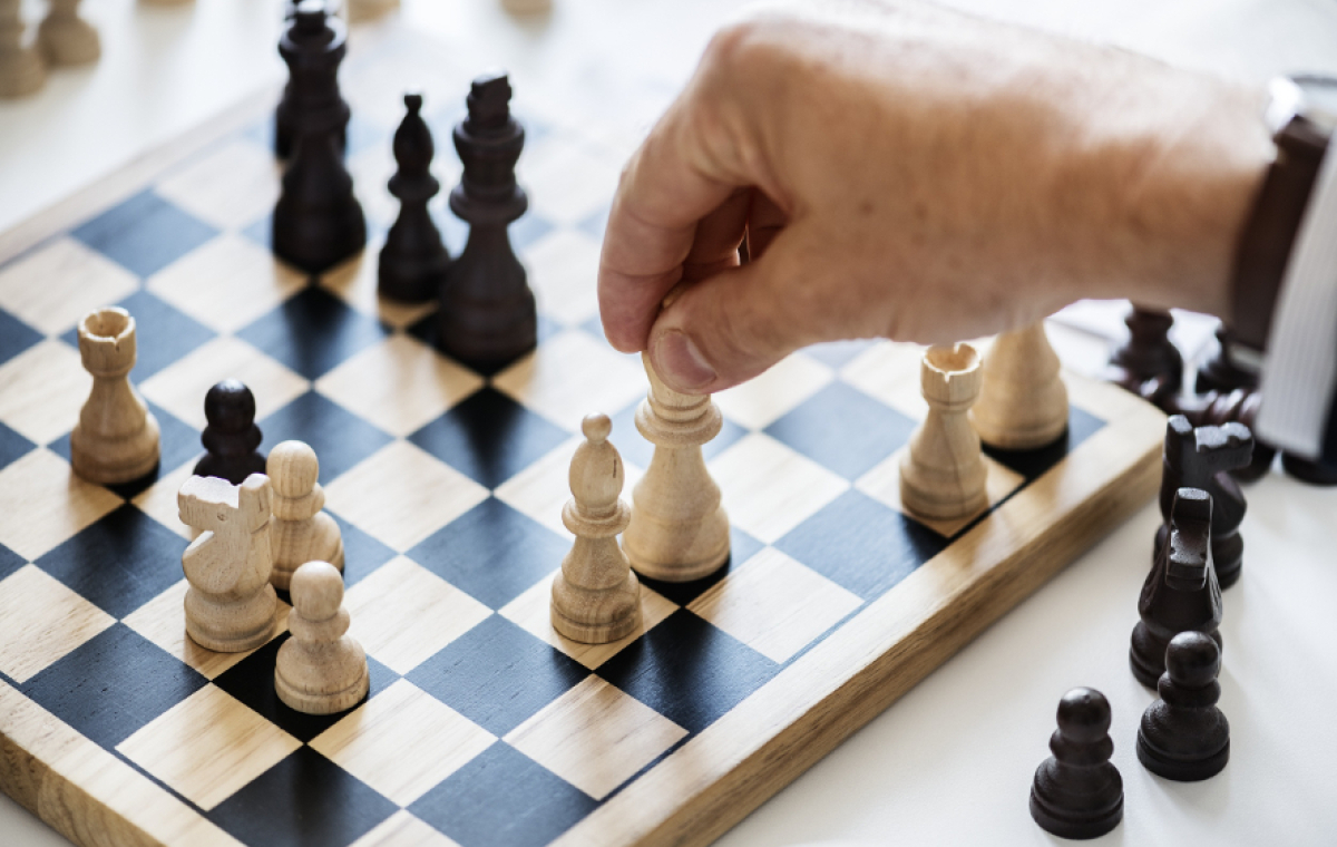 Die Hand einer älteren Person hält eine weiße Schachfigur auf einem Spielbrett
