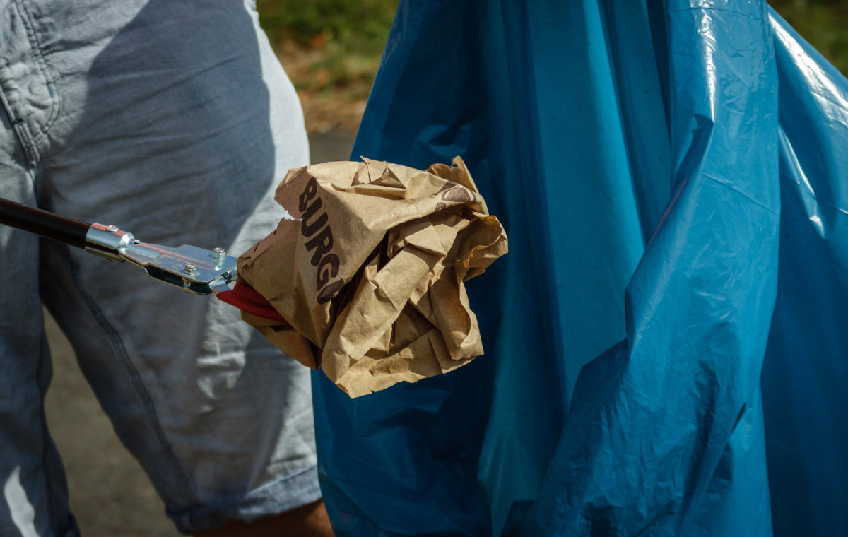 Eine leere Fastfood-Tüte wird mit einer Greifzange in einen blauen Müllsack gelegt.