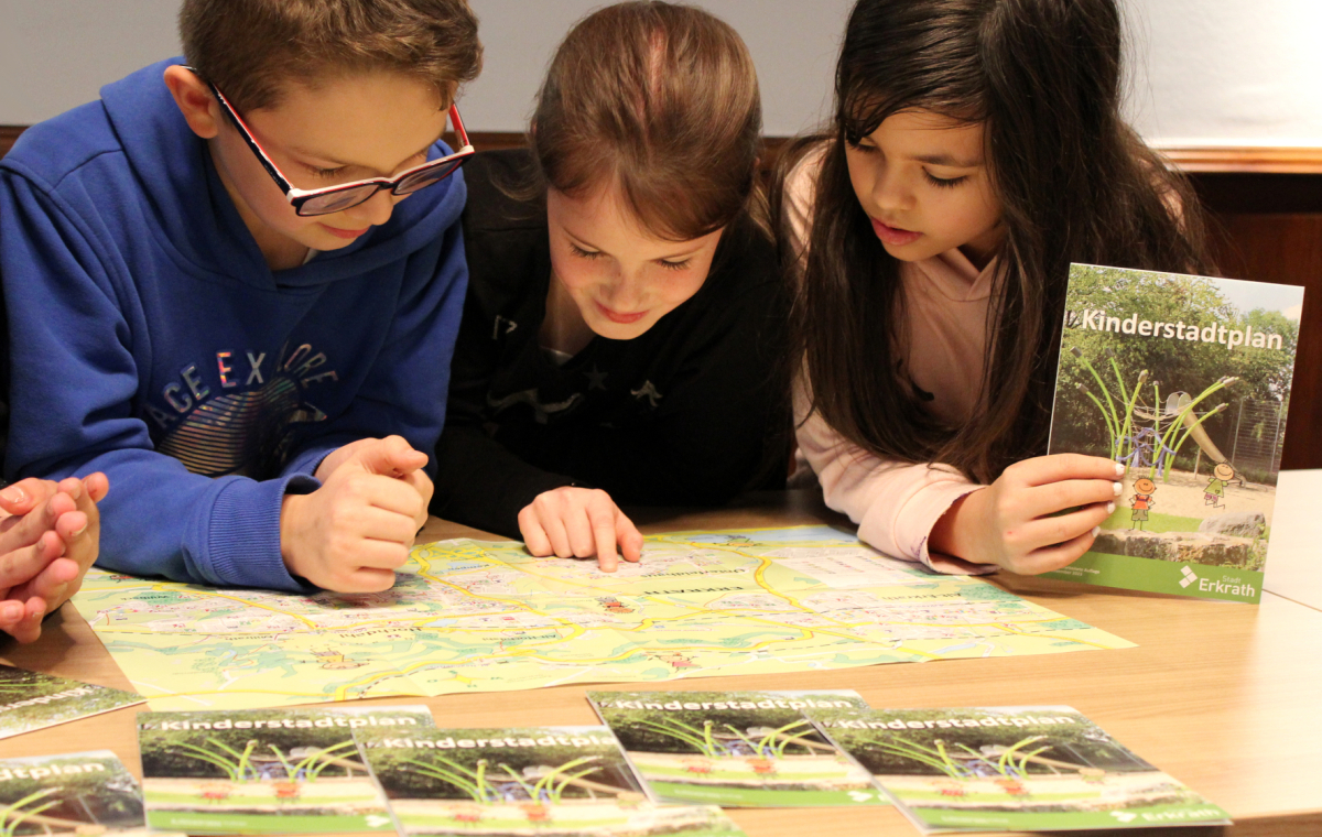 Zwei Mädchen und ein Junge schauen in den Kinderstadtplan der Stadt Erkrath.