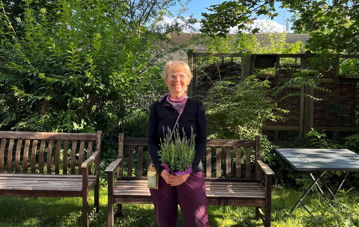 Anemone Hansen mit einem Lavendel in der Hand vor einer Holzbank