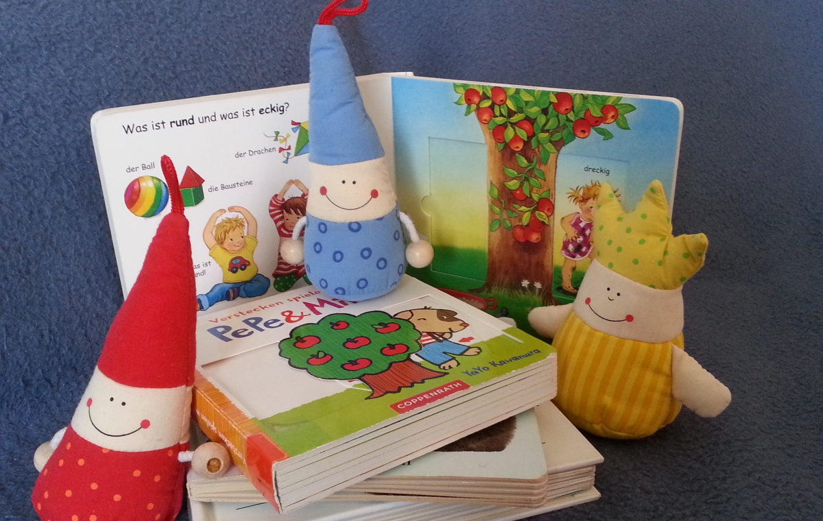 Drei bunte Lesezwerge-Puppen sitzen auf und neben Bilderbüchern