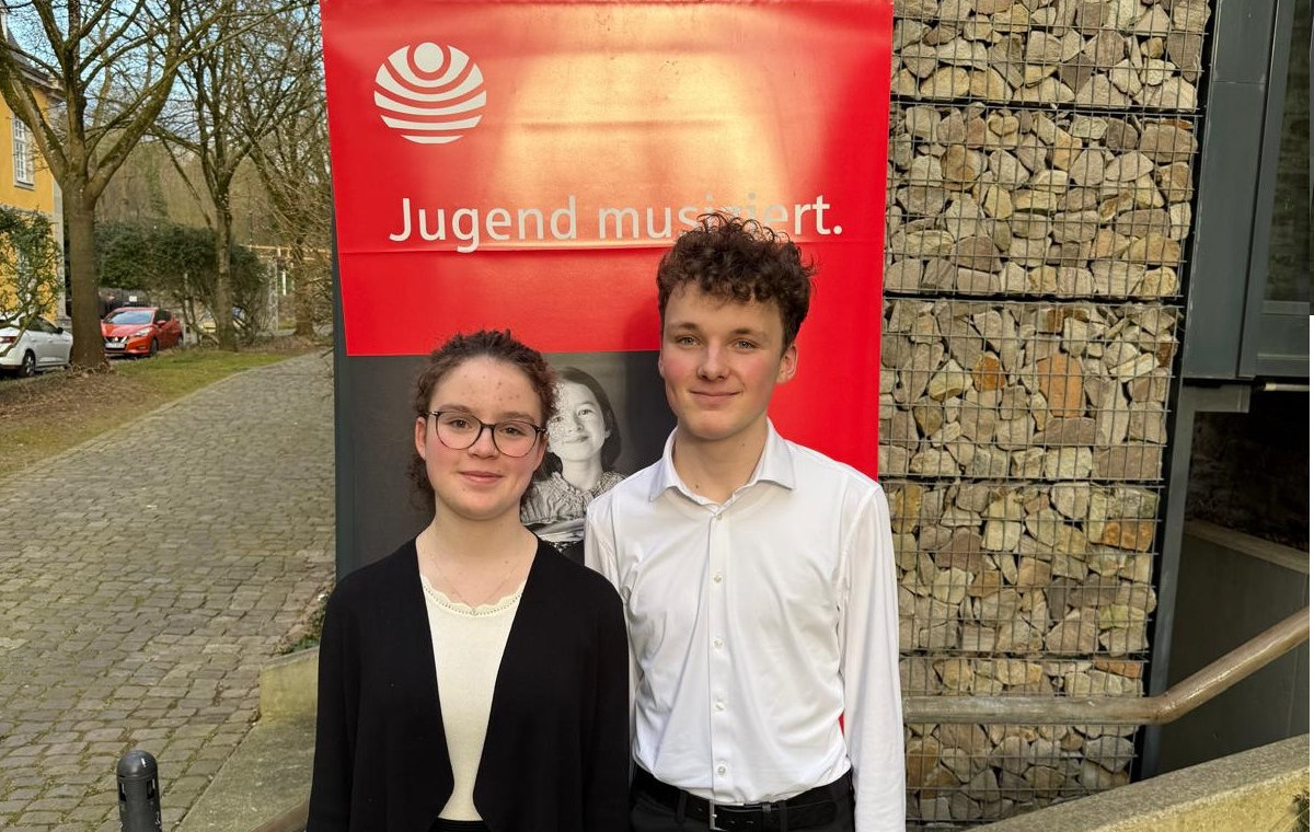 Die Geschwister Sophia und Jonas Amelingmeyer stehen vor einem Banner des Landeswettbewerb „Jugend musiziert“ in Essen.