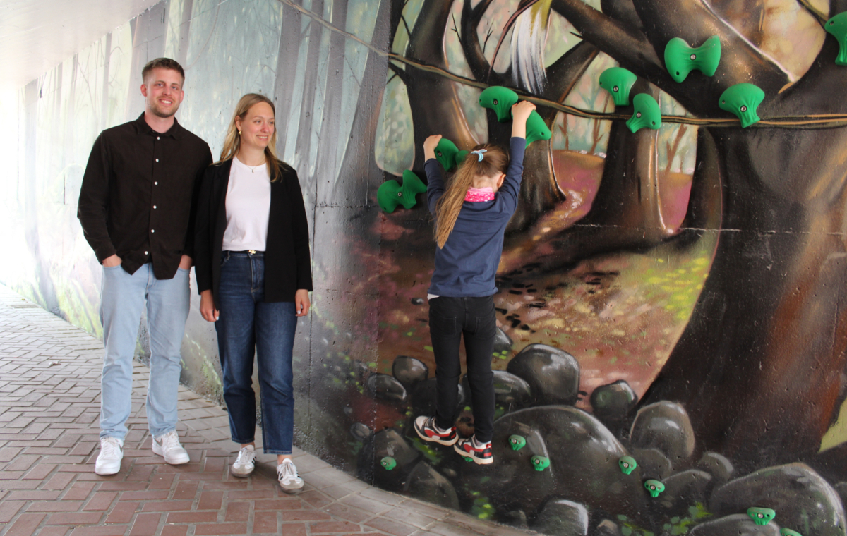 Citymanagerin Katharina Salzburg (M.) und Ludwig Overmann (l.) von der Abteilung Grün in der neugestalteten Unterführung in Hochdahl, die gerade von einem Kind beklettert wird.