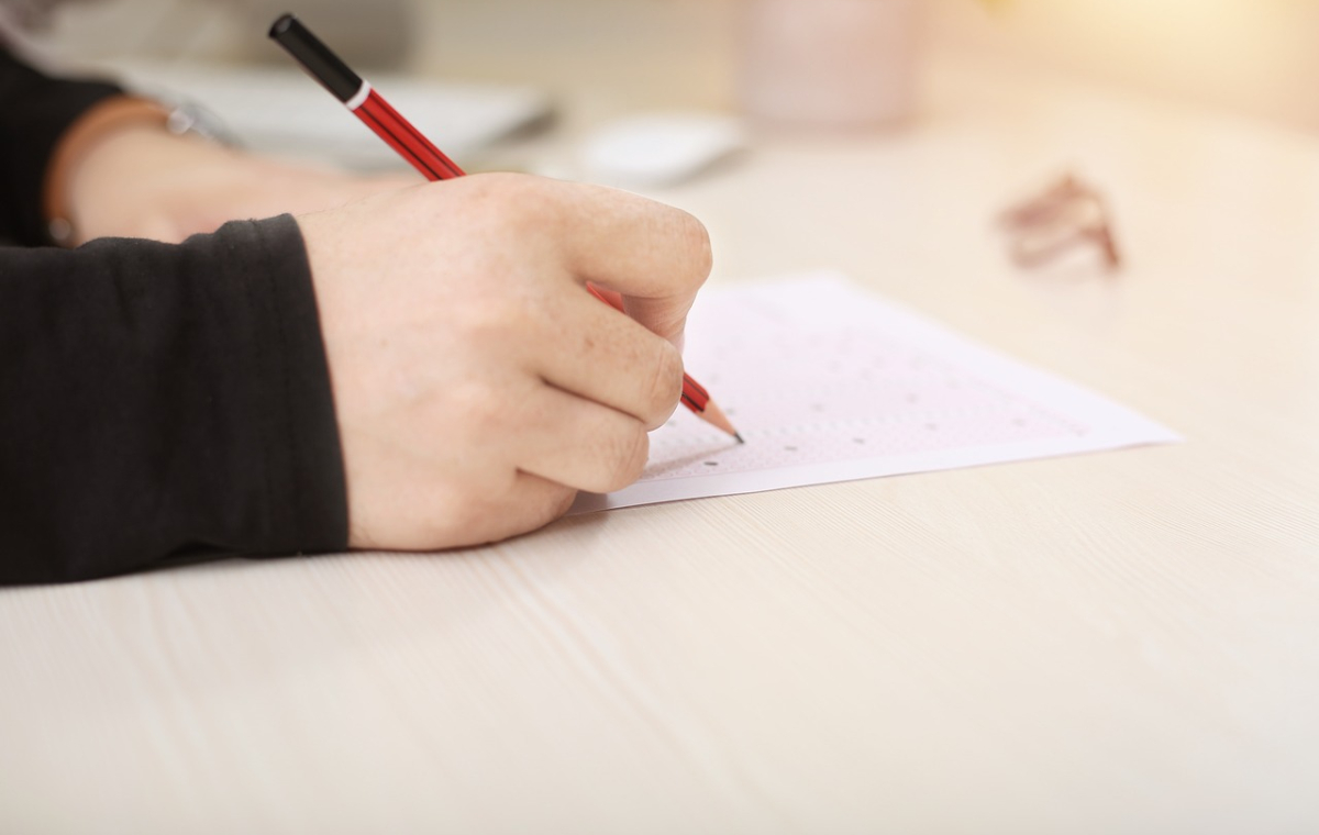 Eine Person füllt mit einem Bleistift ein Quiz aus auf einem Holztisch