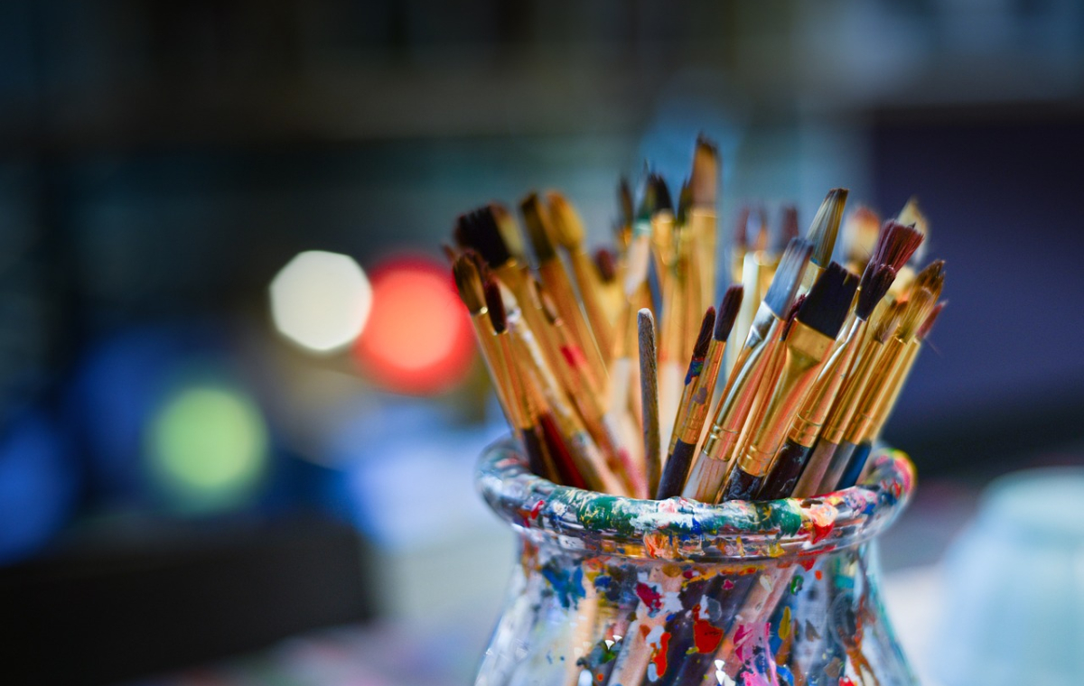 ein mit Farbe bekleckstes Glas, welches voller Pinsel ist
