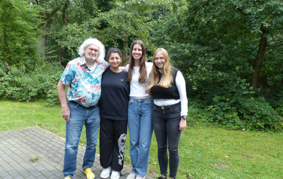 Ein Mann und drei junge Frauen stehen zusammen im Grünen.